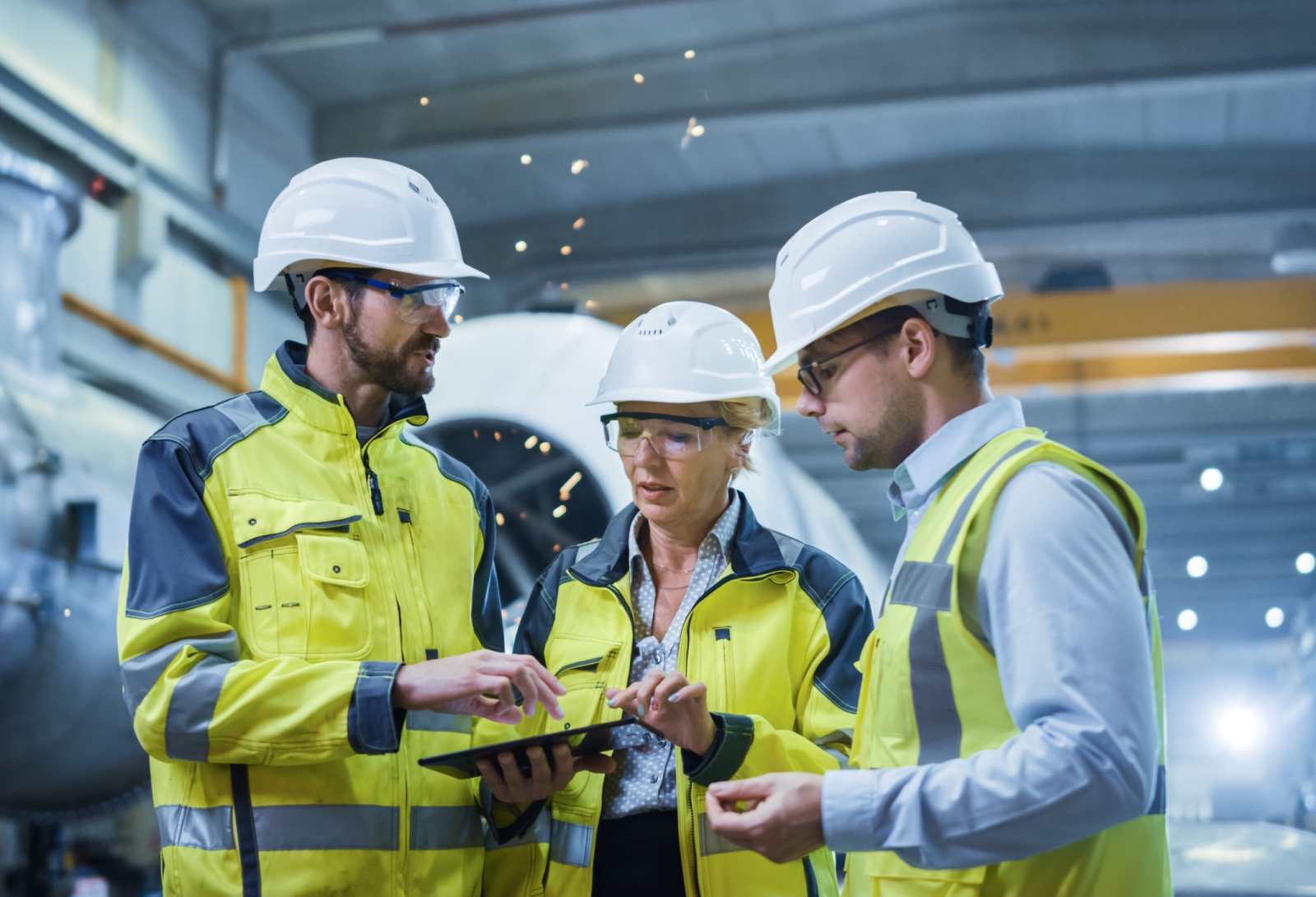 Three Heavy Industry Engineers Stand in Pipe Manufacturing Factory, Use Digital Tablet Computer, Have Discussion. Large Pipe Assembly. Design and Construction of Oil, Gas and Fuels Transport Pipeline